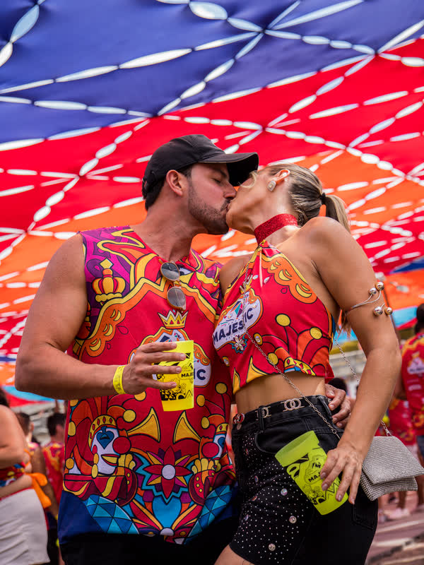 Casal com abadá do Majestic se abraça sob a lona vermelha e azul do camarote.